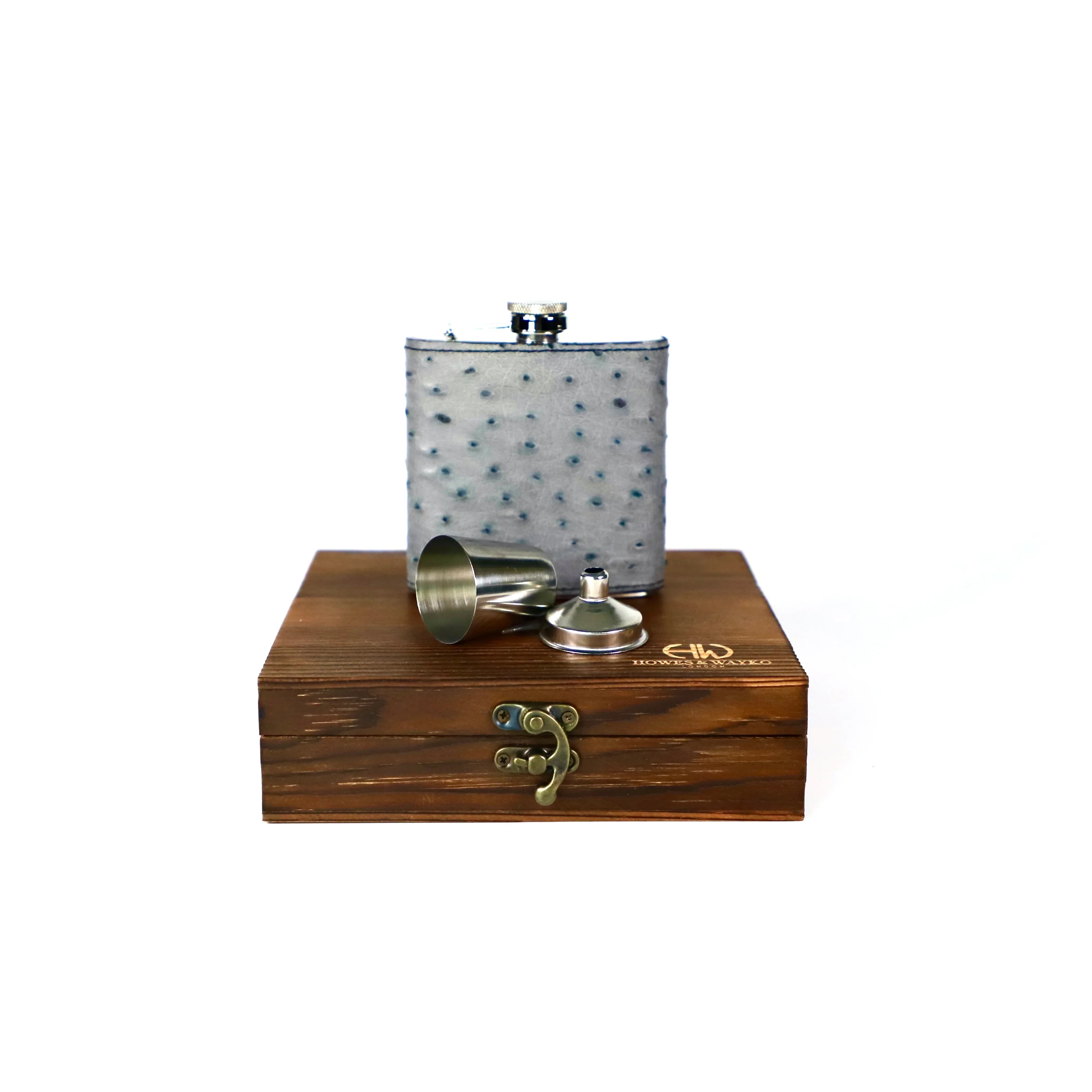 Flask with grey Ostrich skin and accessories on a wooden box against a white background