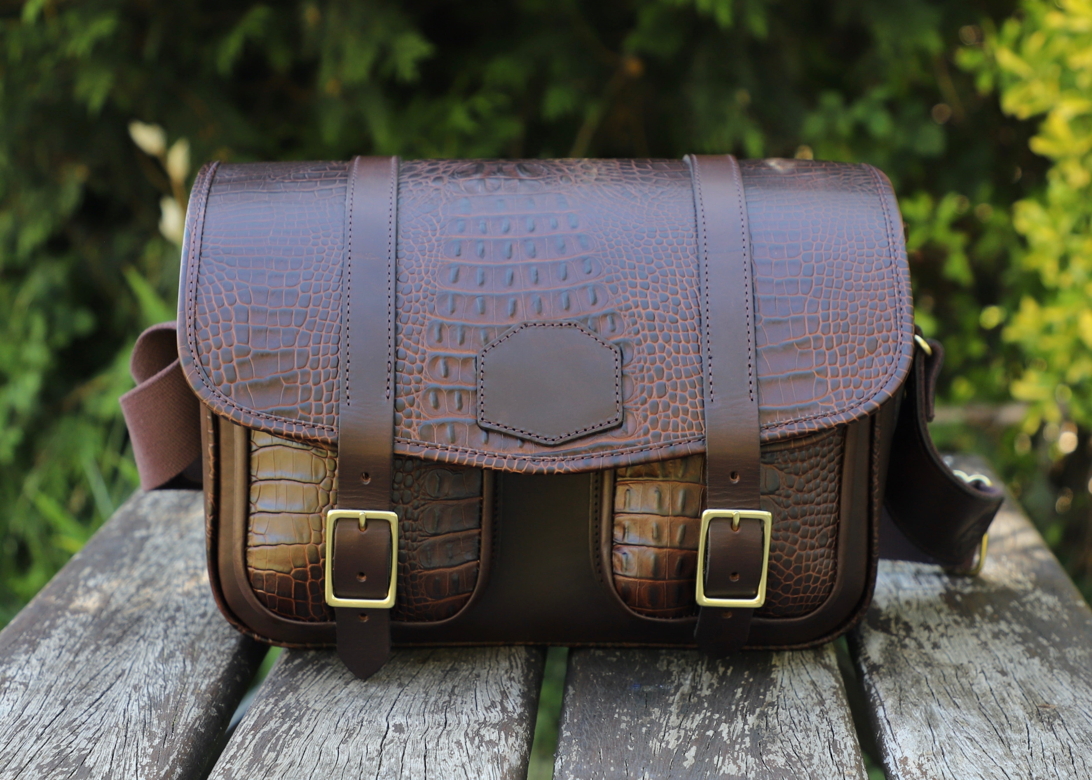 brown mock croco range bag, front view on a wooden table with greenery in the background