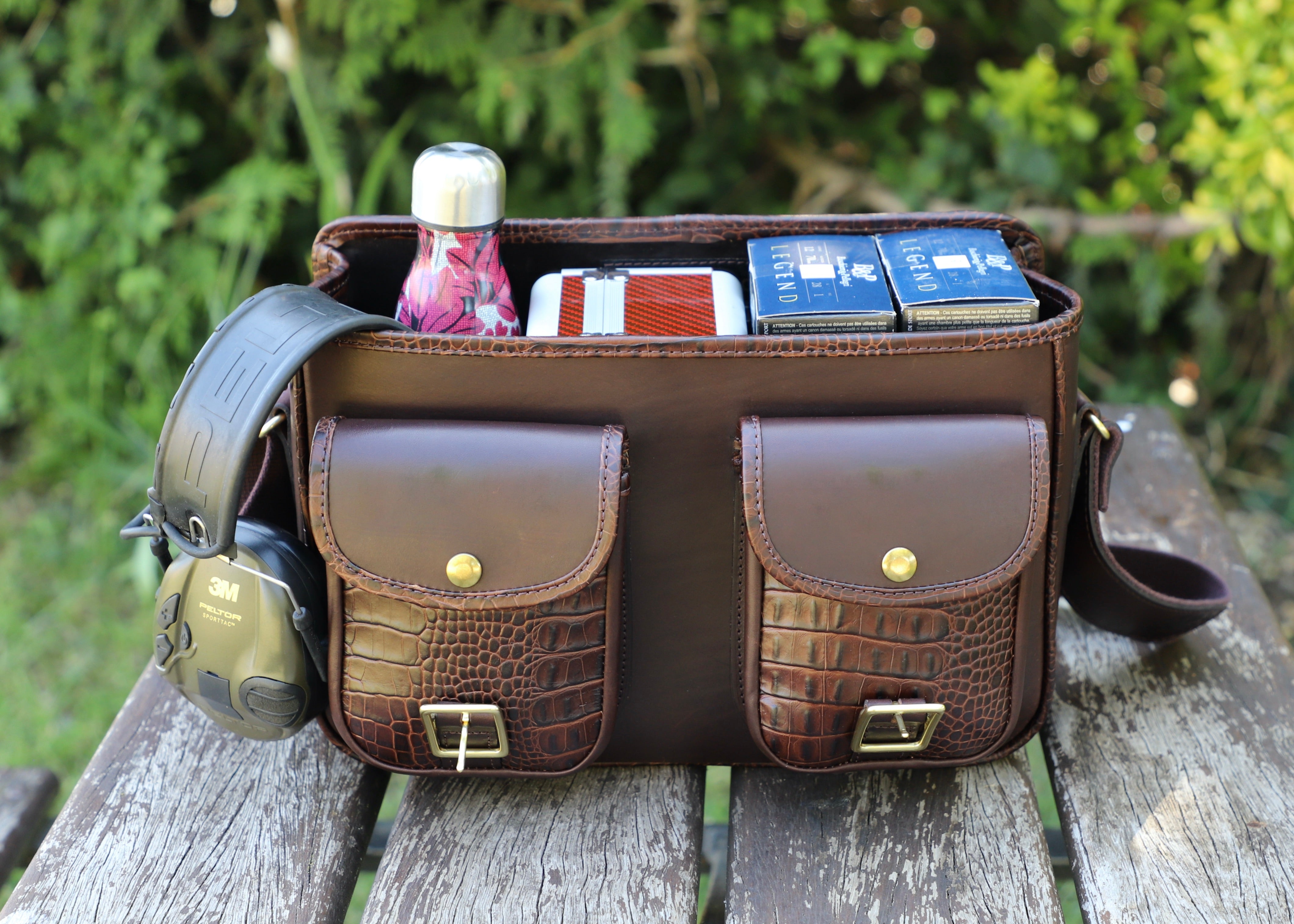 brown mock croco range bag open flaps on a wooden table with greenery in the background