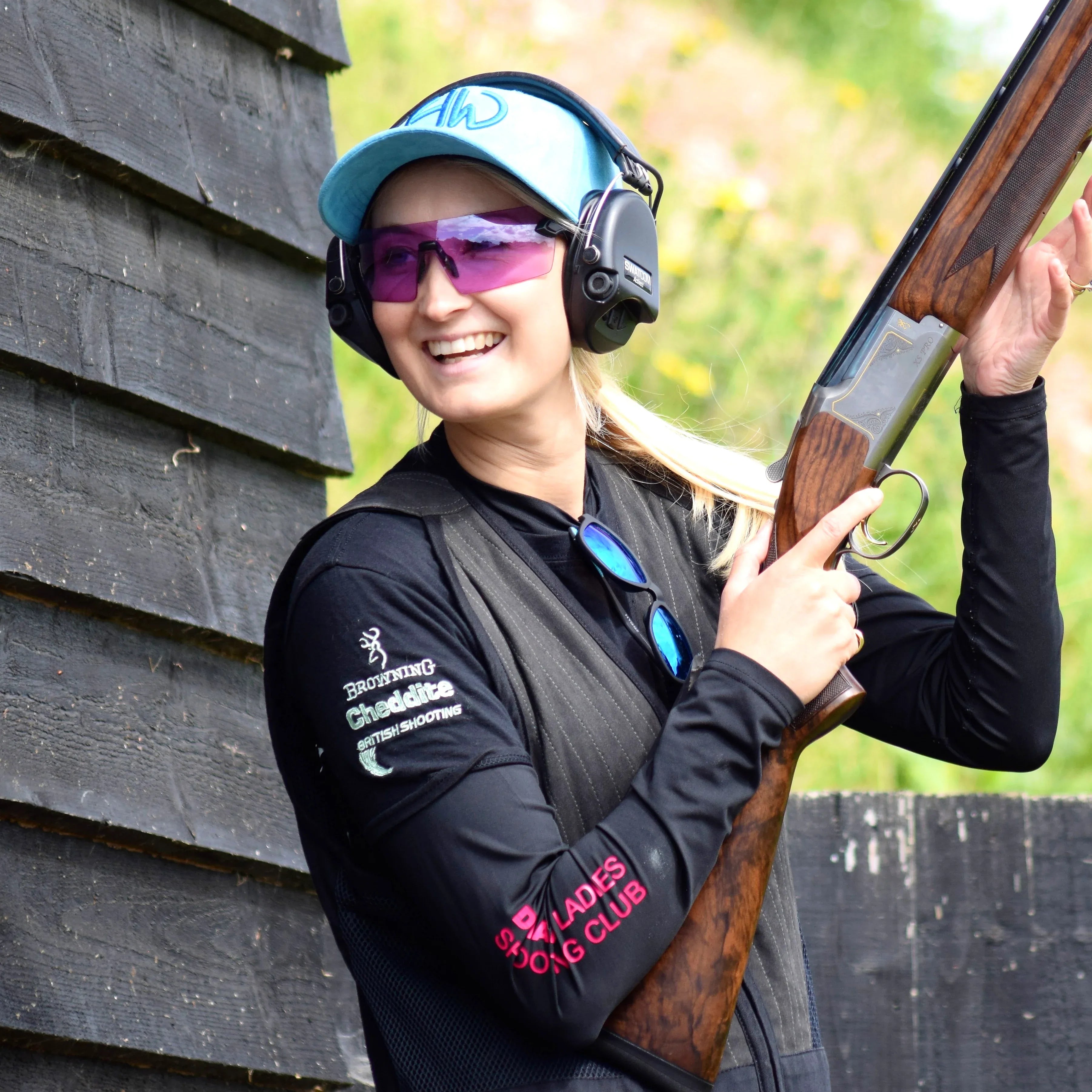 Iris Azul Shooting Baseball Cap - Shooting Accessories adorned in the outdoors by a woman that is also holding a shotgun and has other shooting accessories on