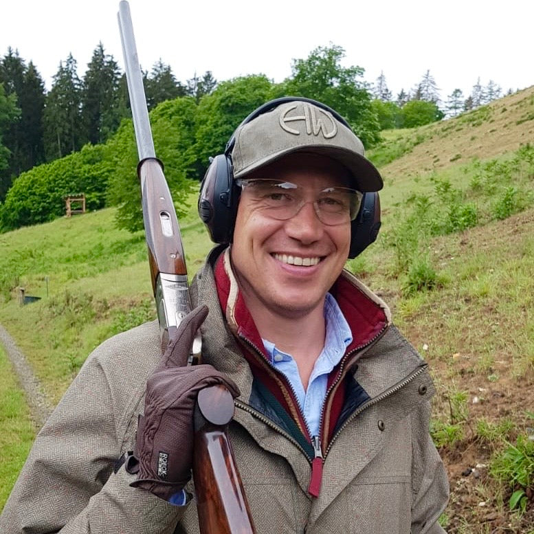 A man at a hunting range wearing an olive green Howes and Wayko baseball cap