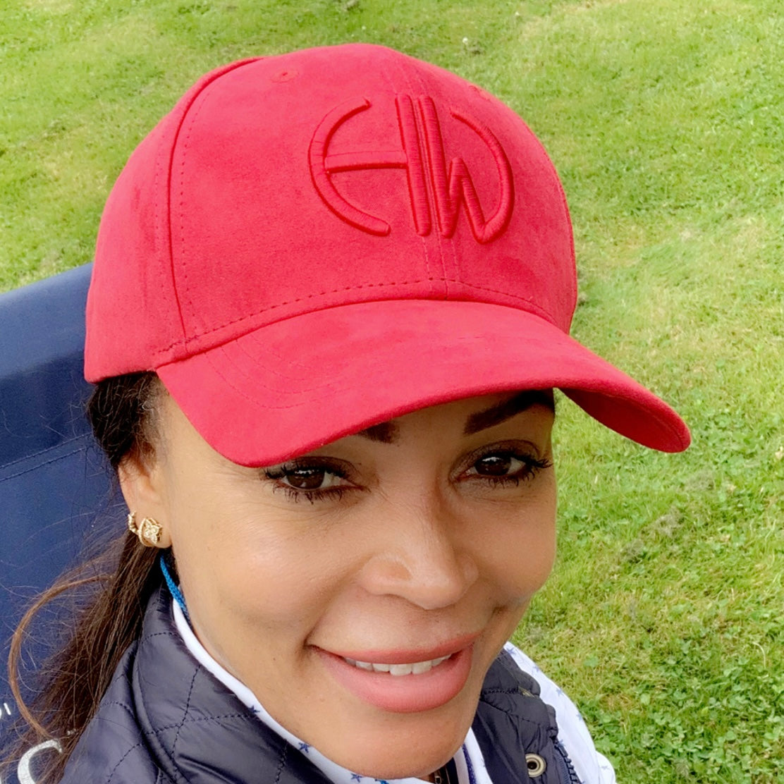 A woman wearing a Howes and Wayko crimson red baseball cap with embroidered logo and a navy gilet with a green background