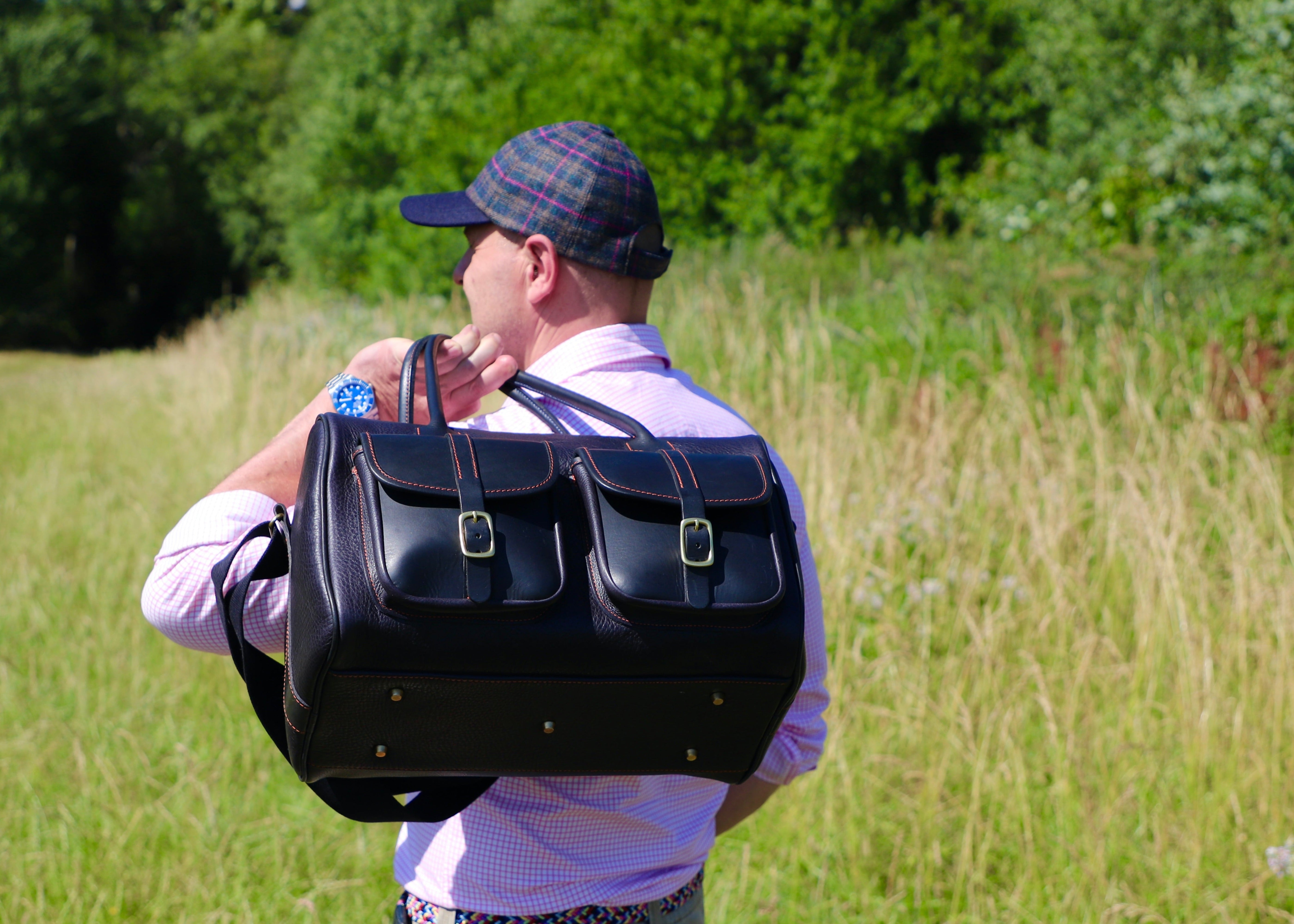 Man carrying a large black bag outdoors in a grassy area