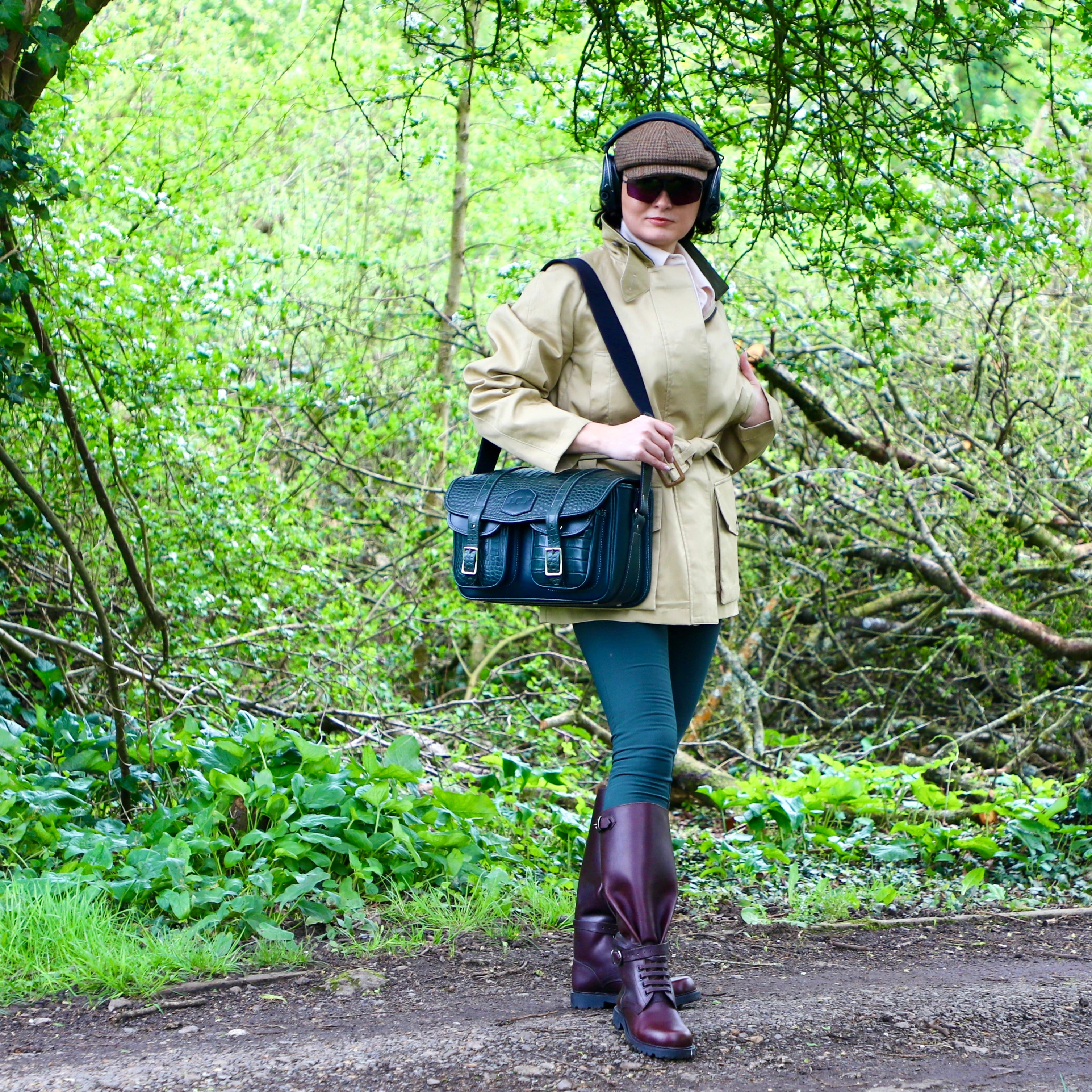 Person walking in a forest wearing a beige coat, blue bag, and purple boots.