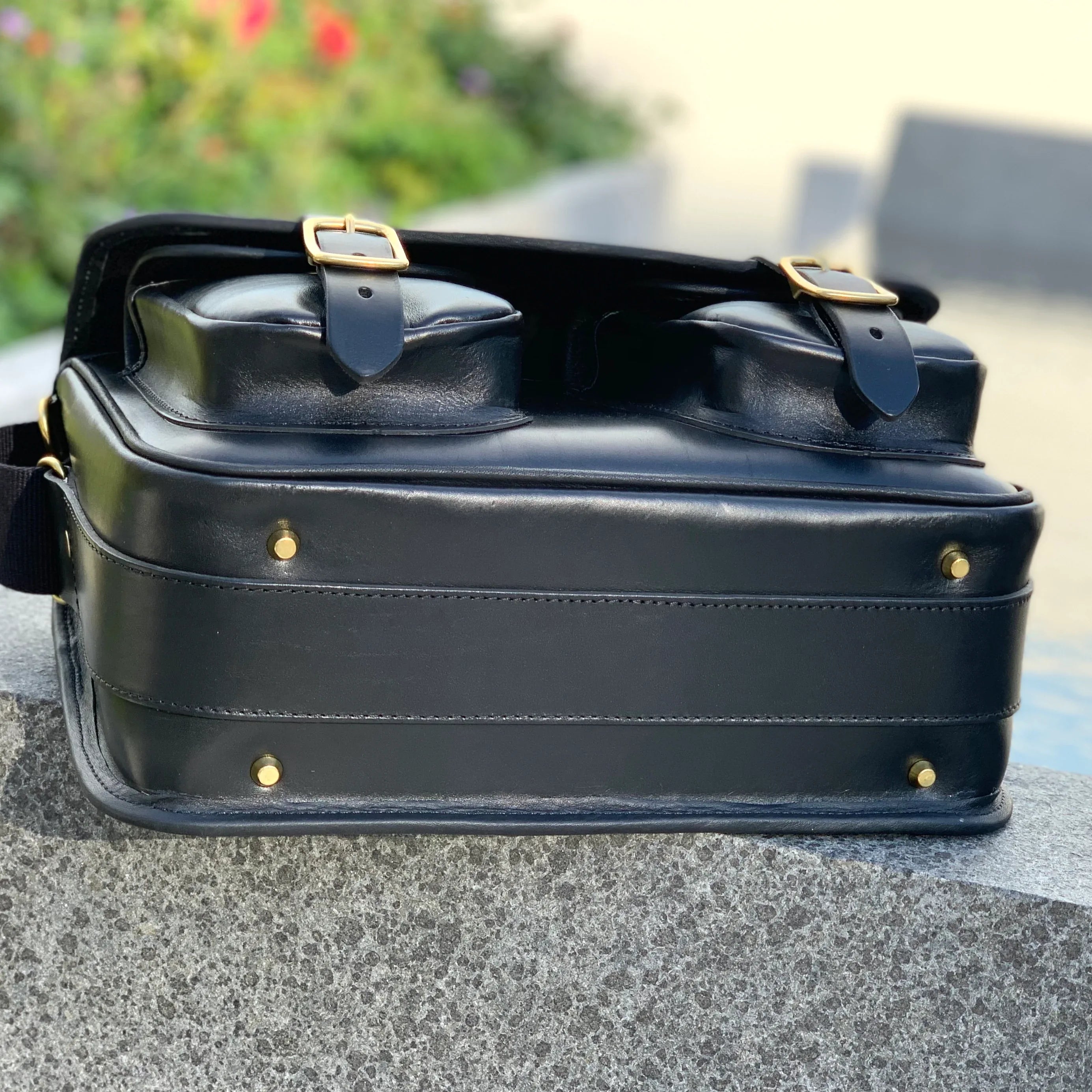 HERA-CELENE BLACK WITH BURGUNDY SNAKE CARTRIDGE BAG bottom view with bag sitting on a wall on its back in the outdoors