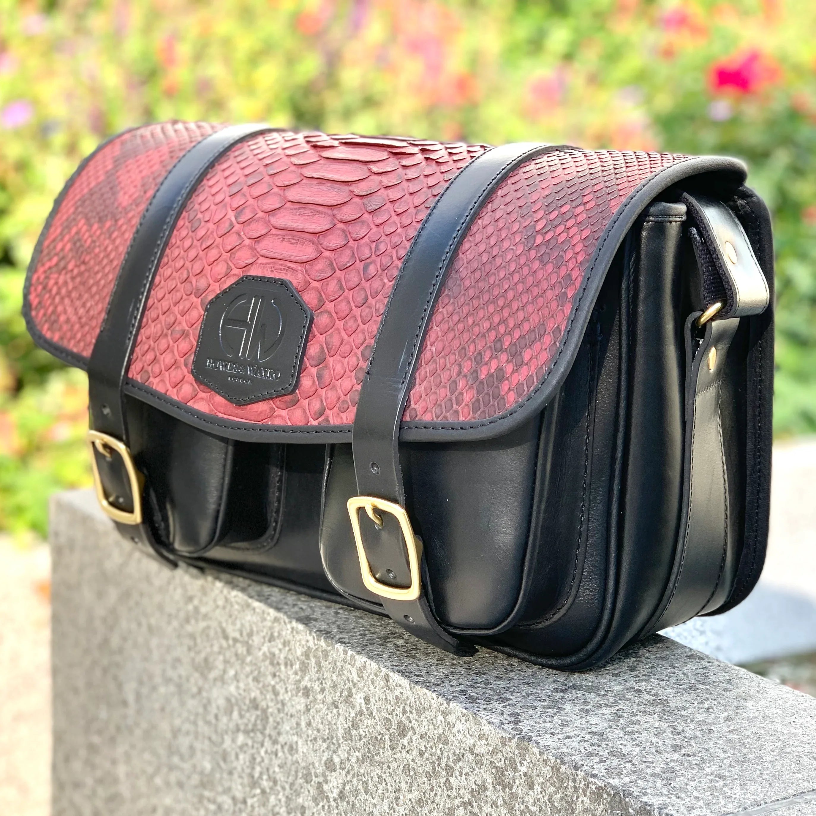 HERA-CELENE BLACK WITH BURGUNDY SNAKE CARTRIDGE BAG side view with bag sitting on a wall in the outdoors