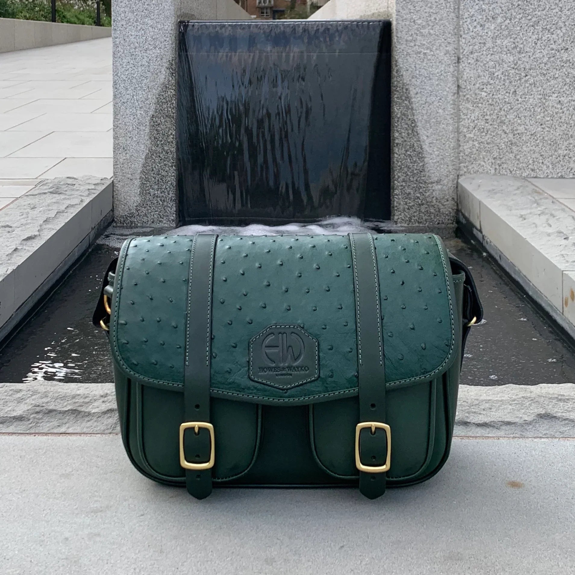 British Made Hera-Eden Green & Ostrich: Shooting Cartridge Bag front view in front of a fountain