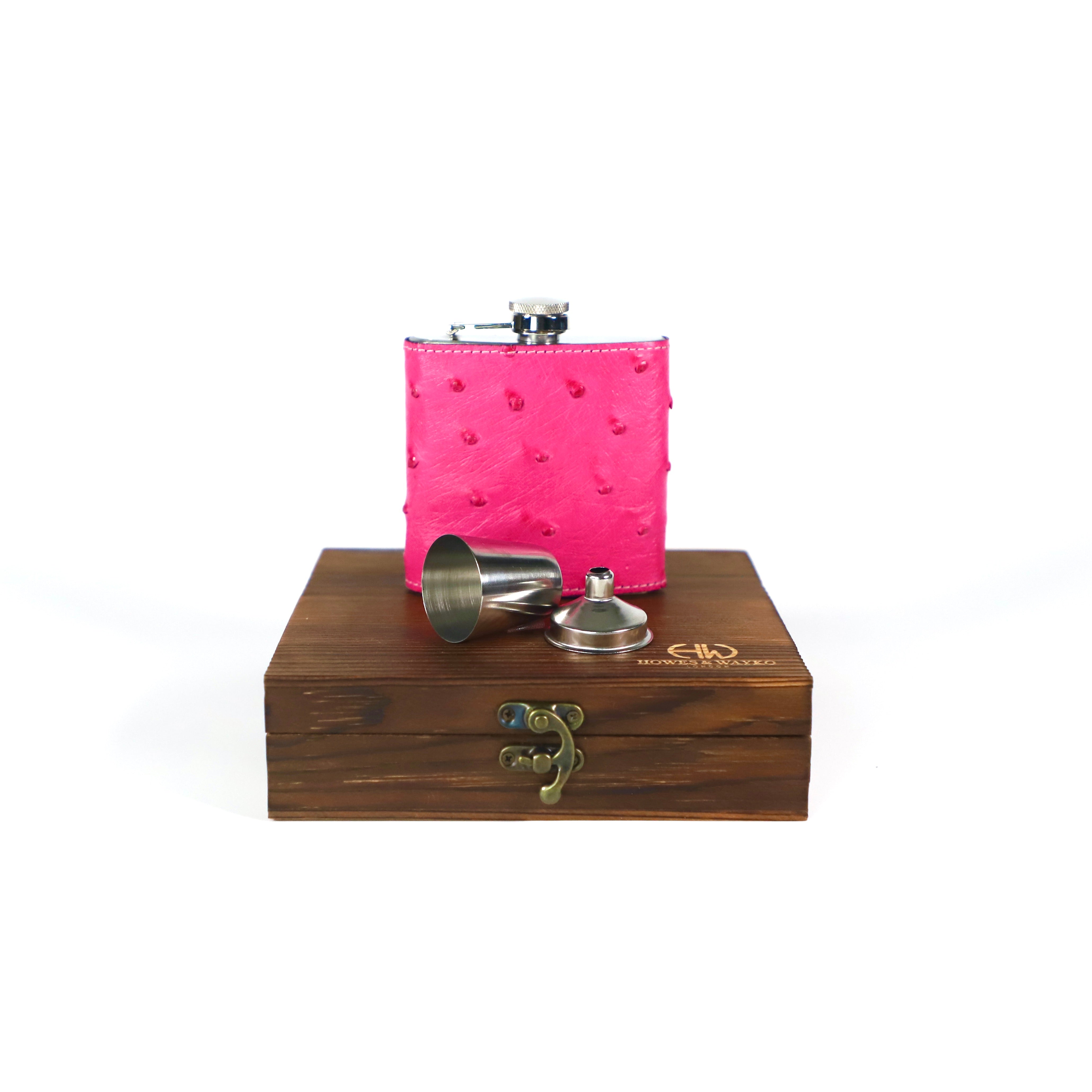 Pink  Ostrich covered flask with silver cap and accessories on a wooden gift box stand with Howes and Wayko's branding.