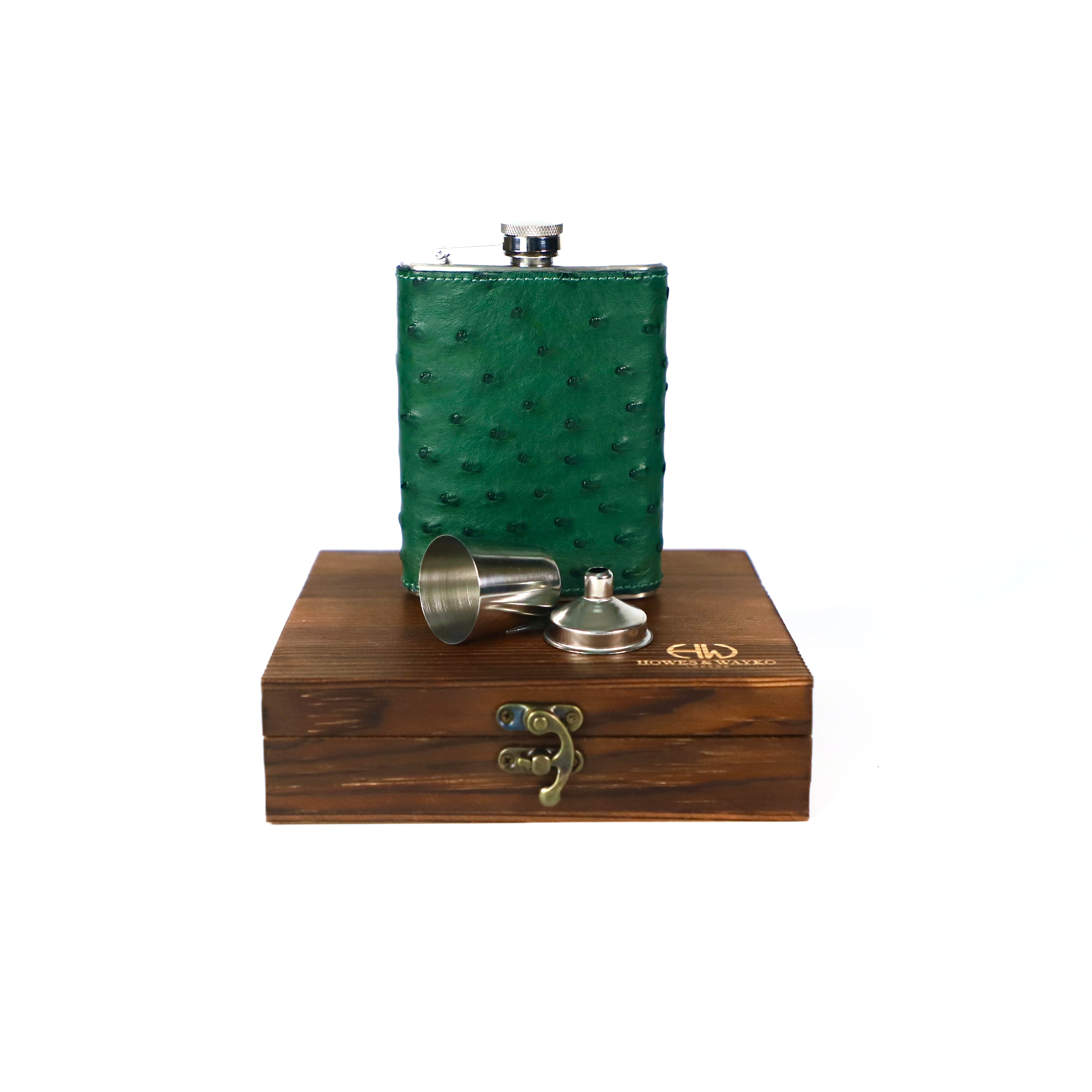 stainless steel hip flask, covered with green Ostrich leather, displayed on a brown wooden gift box displayed with a white background.