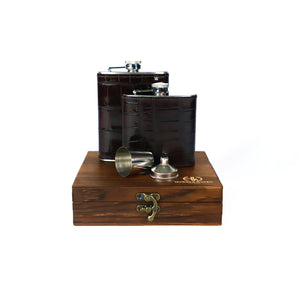 Two dark  moc-croc leather flasks with silver caps on a wooden stand with a white background