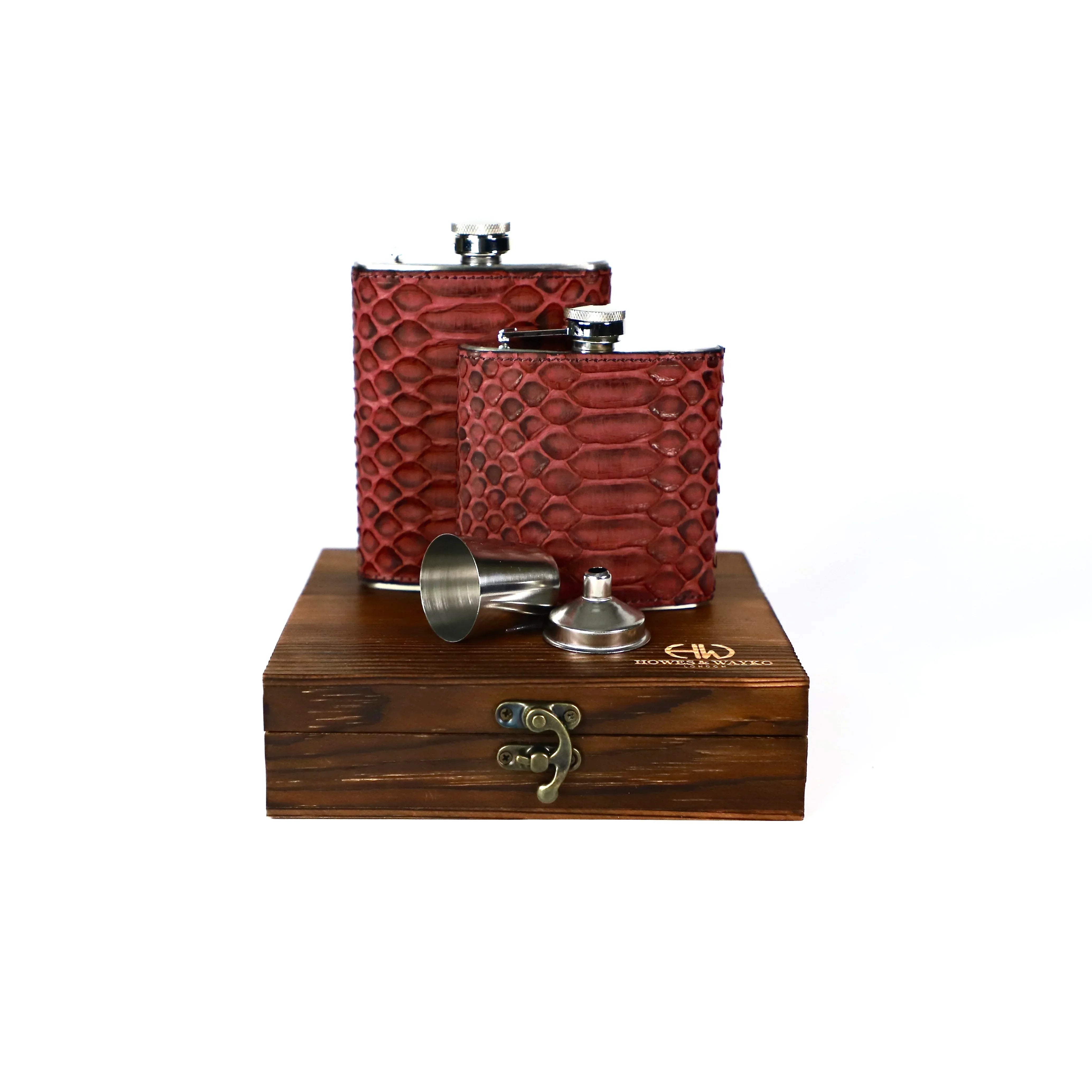 Two Stainless steel flasks, covered in burgundy snake leather, were displayed on a wooden gift box alongside a stainless steel shot glass and a funnel. This has a white background.