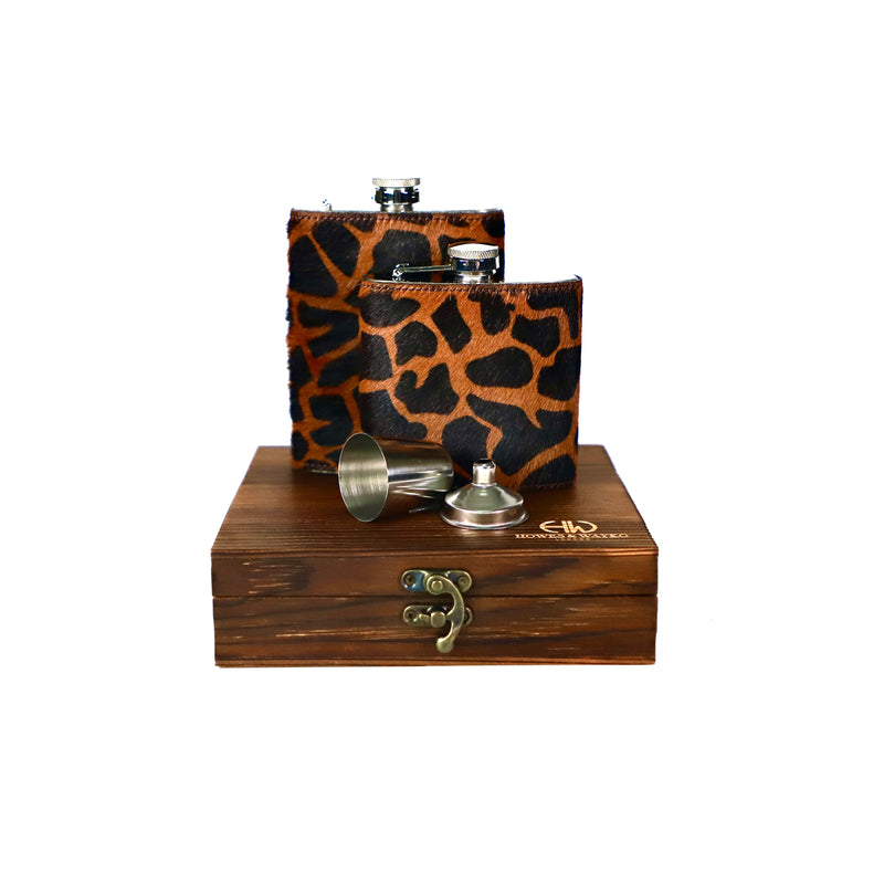 Silver hip flask covered with a giraffe print leather on a wooden box against a white background