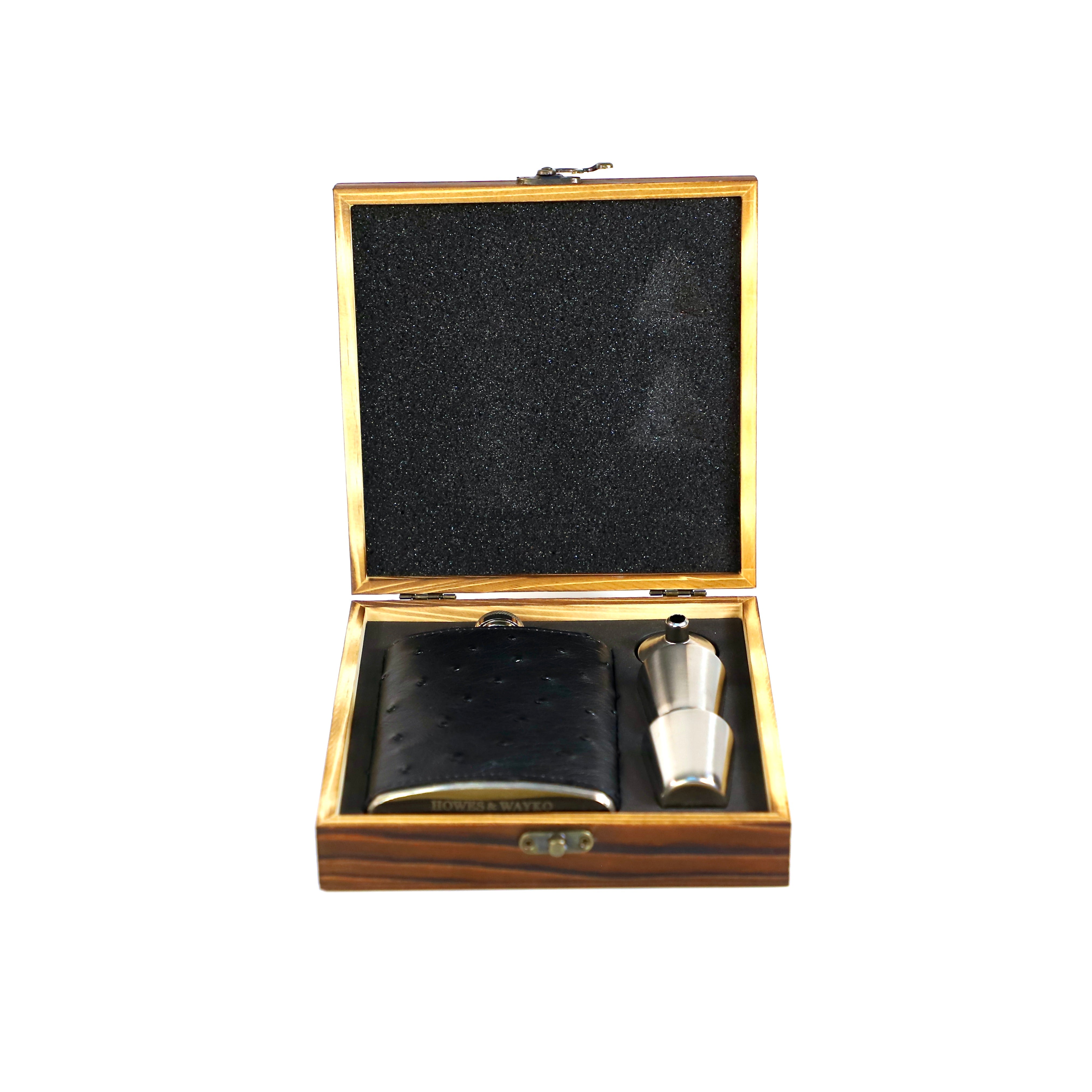 Hip flask covered in black Ostrich skin, displayed in a wooden gift box, alongside a pair of shot glasses and a funnel.