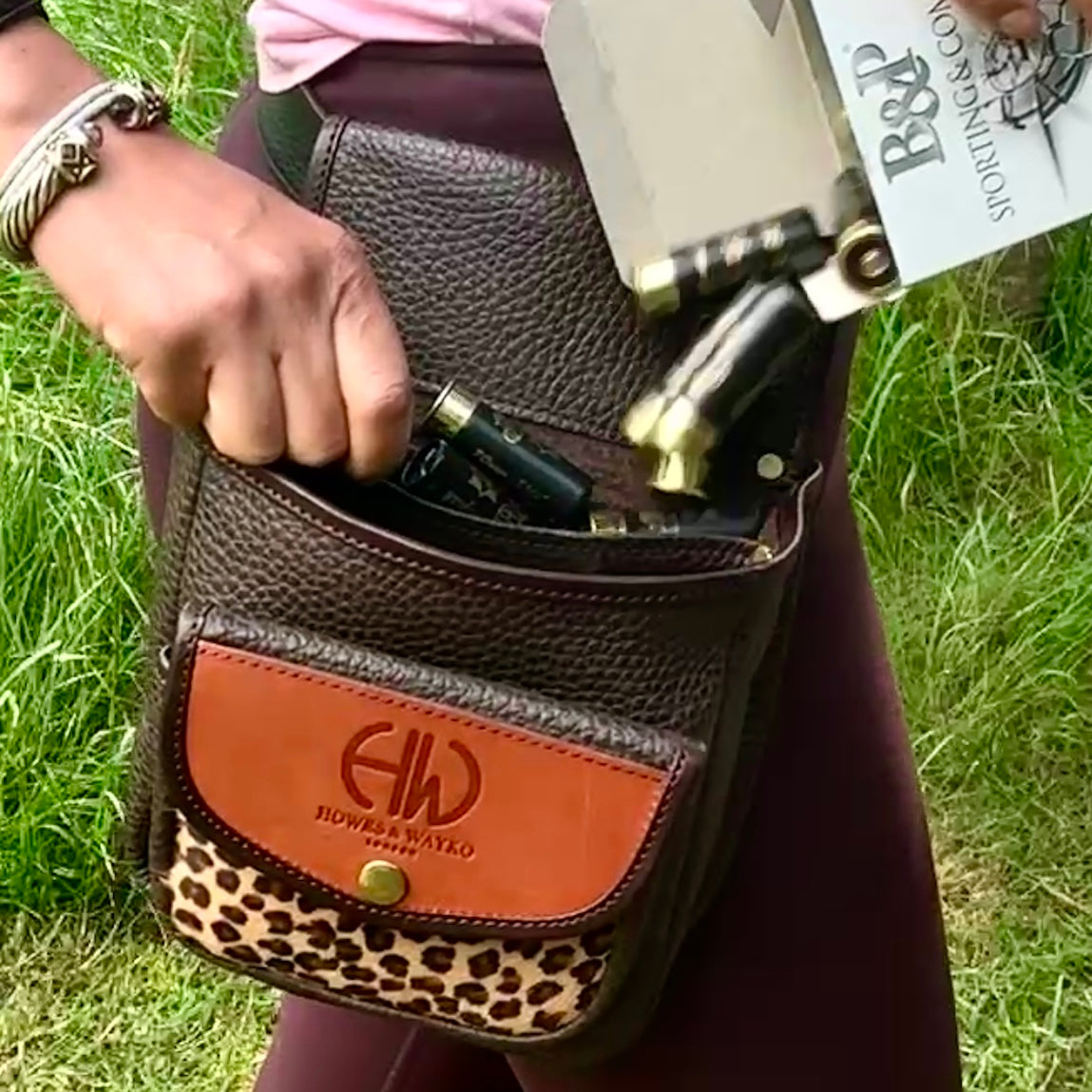 Brown leather bag with leopard print detail held by a person on the grass