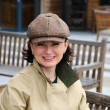 British Made HESTIA Gatsby Tweed Cap adorned on a woman sitting down on a bench smiling