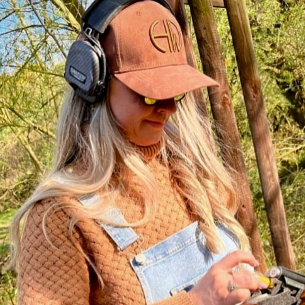 A woman wearing a brown Howes and Wayko logoed cap, headphones, and sunglasses outdoors.