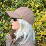 GAIA - Latte Wool Shooting Baseball Cap being adorned on a woman outdoor with greenery/bushes in the close background