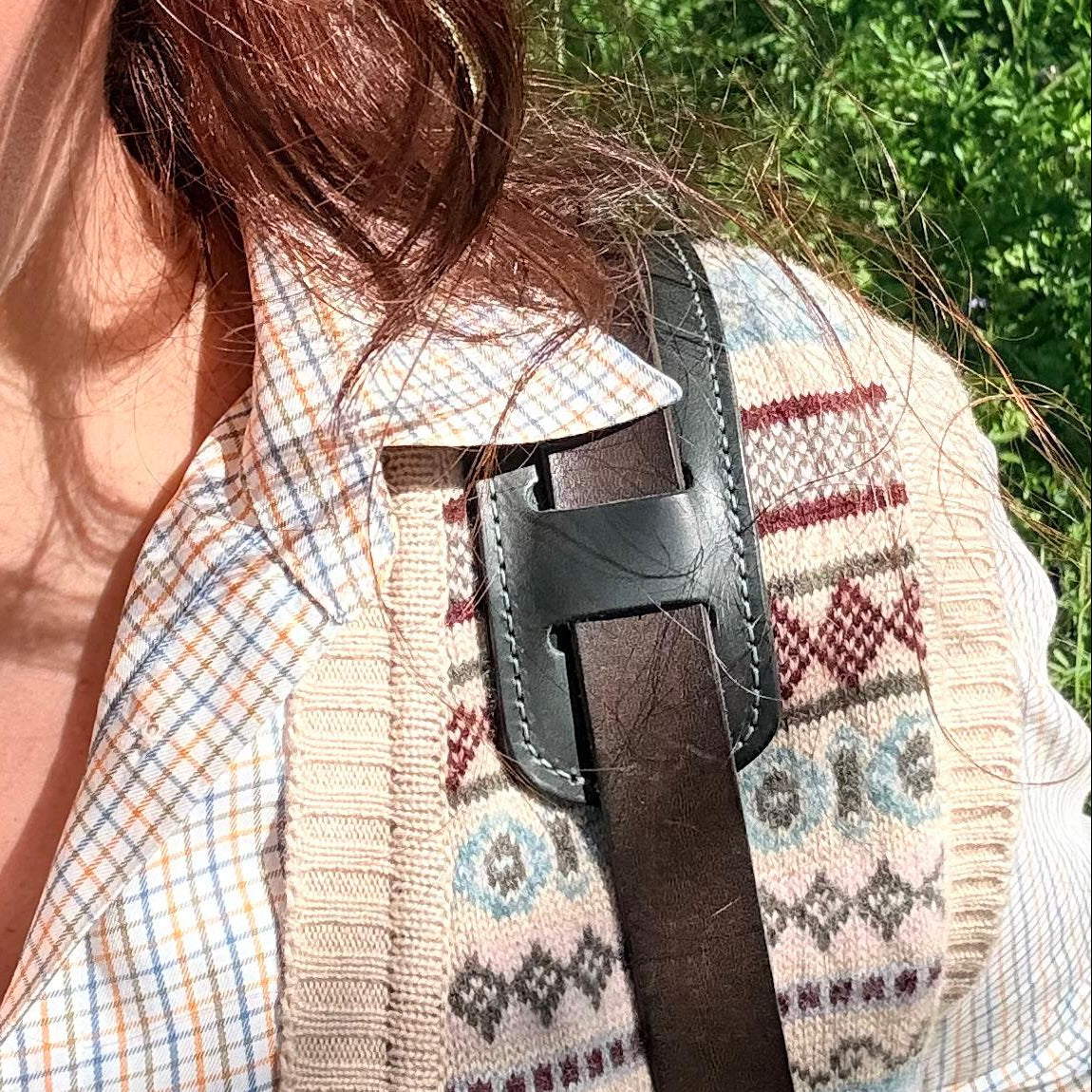 A person wearing a patterned shirt with a green strap over their shoulder outdoors