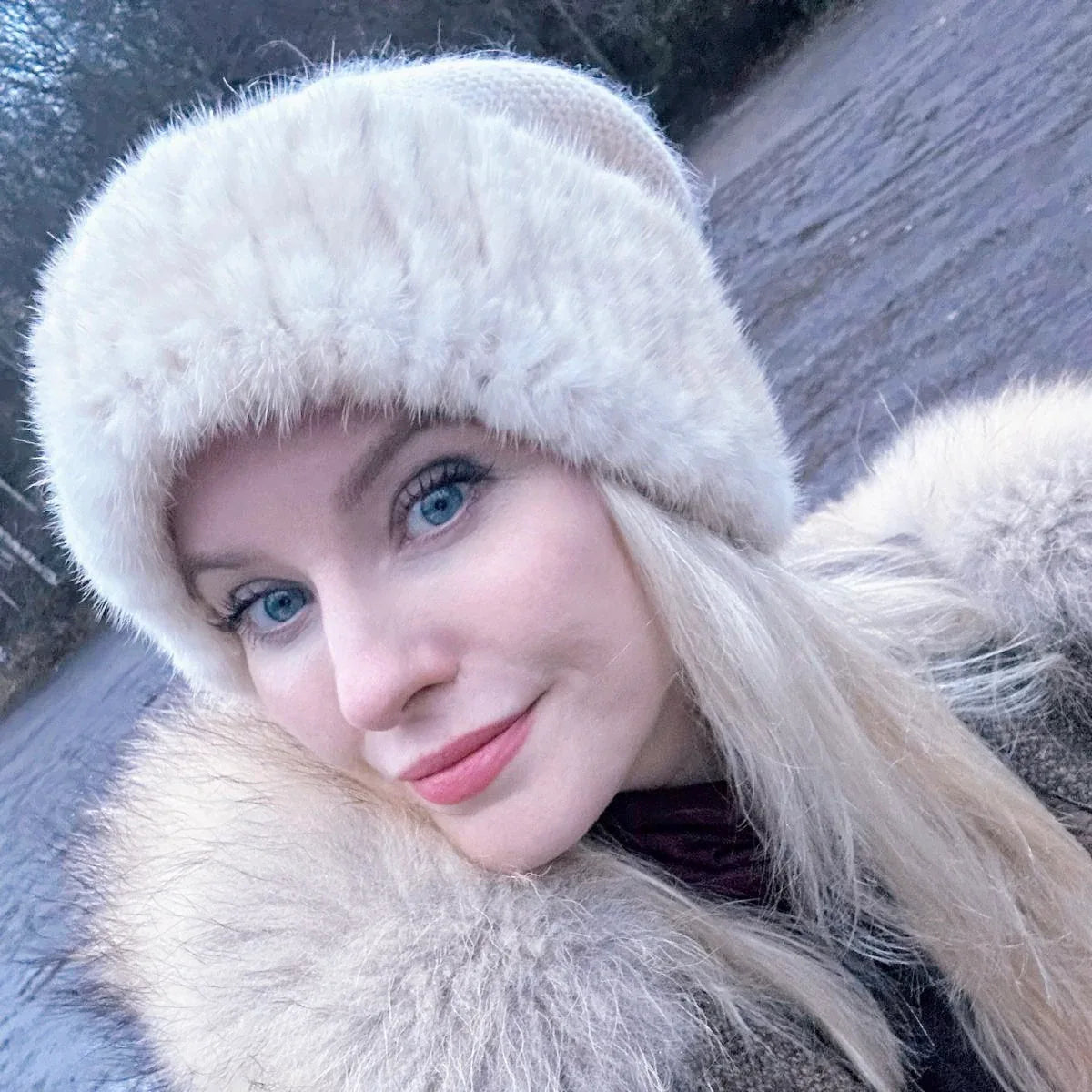 Woman wearing a white fur beanie hat and coat in a snowy outdoor setting