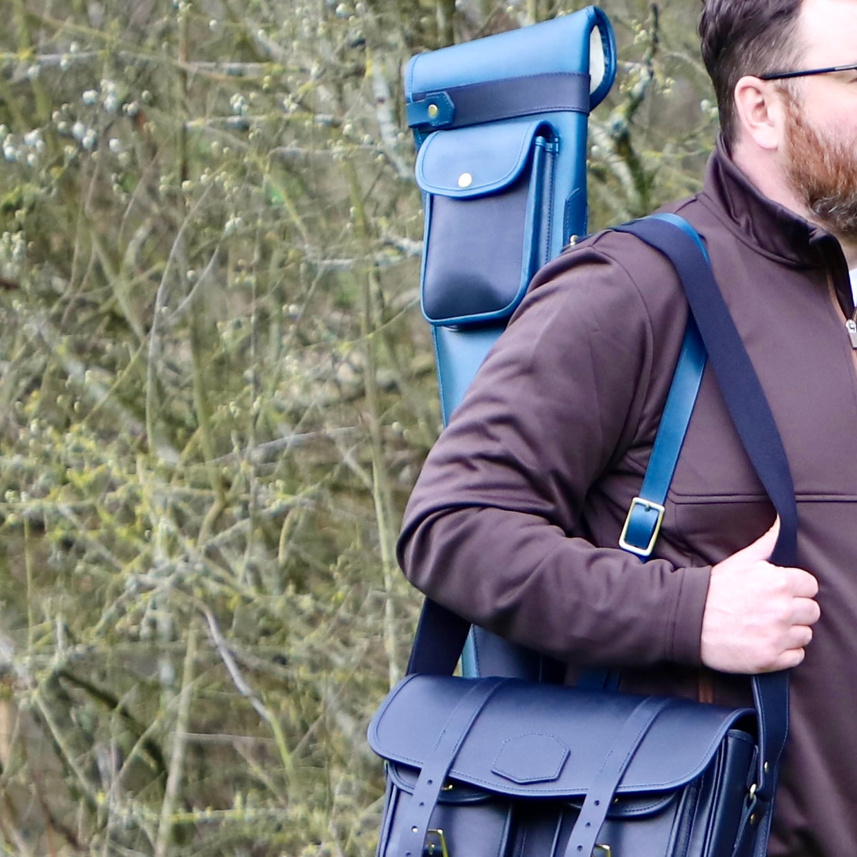 A man carrying a Howes and Wayko blue leather slip with a forest background