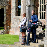 woman and man standing with shooting accessories including cartridge bags, and gun slip. image taken outside an old building