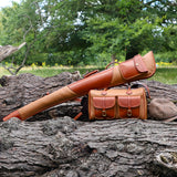 Leto-Tan Gun Slip - Fleece Lined Leather Gun Protector in the woods resting on fallen wooden logs and next to a matching cartridge bag and tweed cap