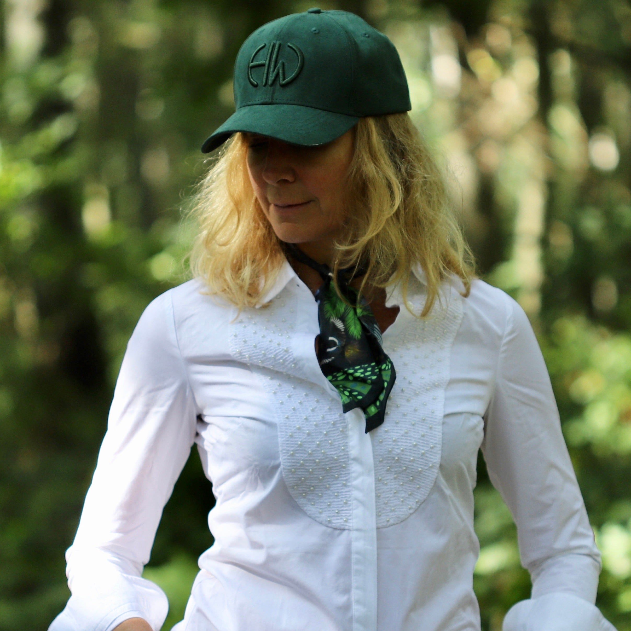 Iris Forest Green Shooting Baseball Cap adorned on a woman in a forest to showcase this hat and other shooting accessories like the twill scarf